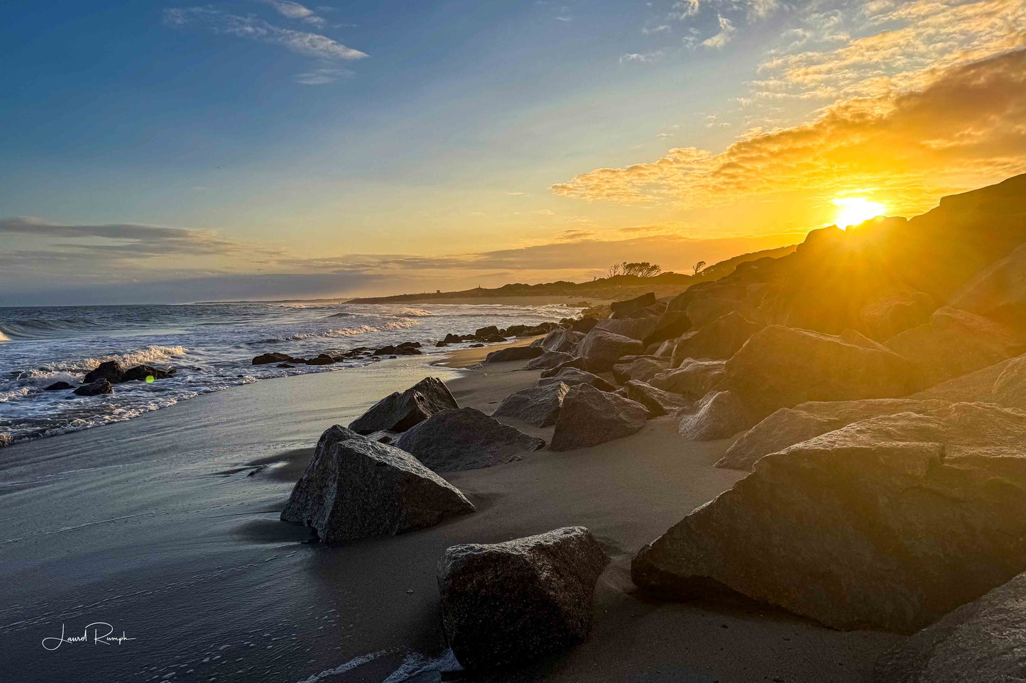 Golden sunset at the Fort Fisher Monument in North Carolina with sunlight peeking through large coastal boulders.