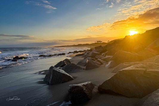 Golden sunset at the Fort Fisher Monument in North Carolina with sunlight peeking through large coastal boulders.
