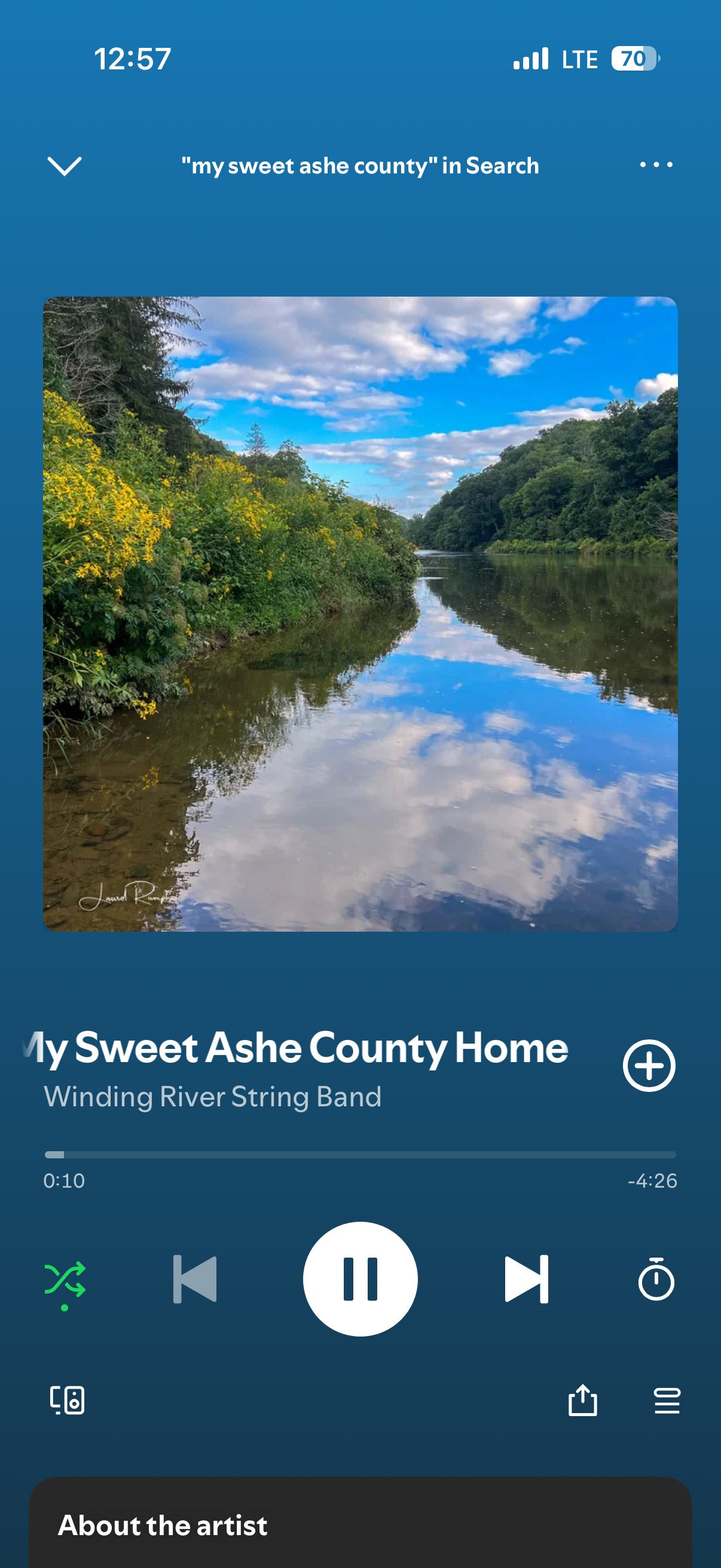 Music app screen showing 'My Sweet Ashe County Home' by Winding River String Band with a scenic background featuring Elk Shoals in Ashe County, North Carolina..