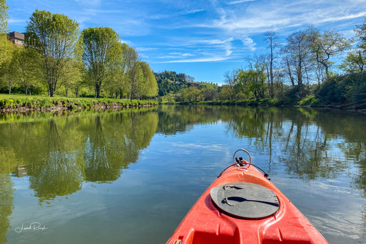 Orange kayak on a calm New River with trees and blue sky in the background in Ashe County, North Carolina.
