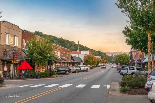 Downtown West Jefferson, North Carolina at golden hour with parked cars, outdoor seating under a large tree, and warm evening light on a small-town street.
