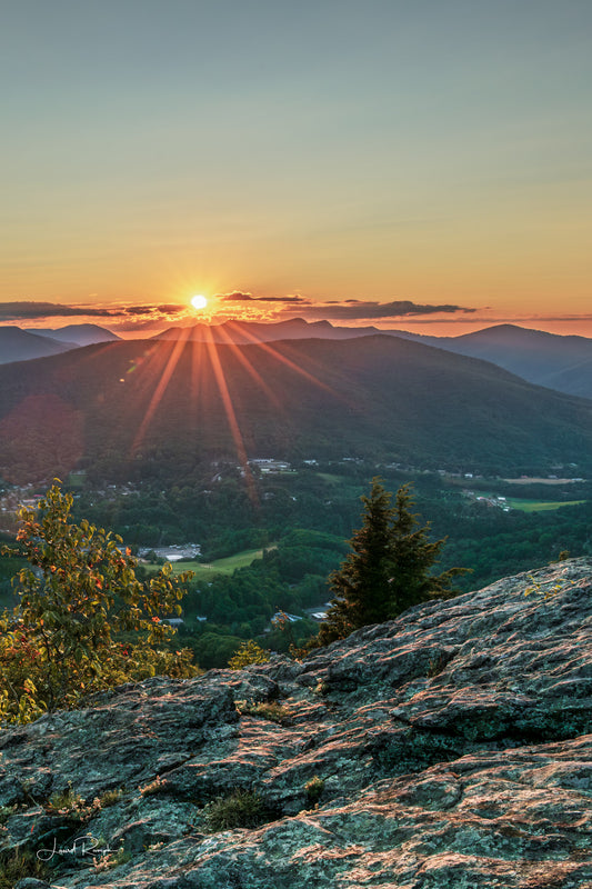 Sunset view from Jefferson overlook on top of Mount Jefferson in Ashe County, North Carolina, where the starburst of the sun is peering from behind three top mountain. 2x3 crop