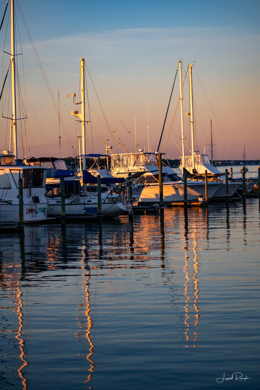 Snows Cut Marina in North Carolina at sunset with sailboats docked and masts reflecting in pink and blue water.
