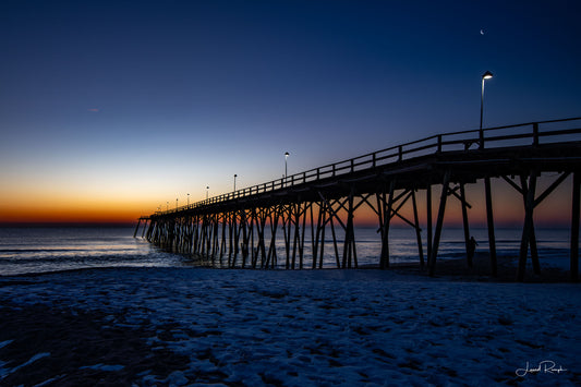 Kure Beach Pier, North Carolina just before sunrise with deep blue and orange color in the pre-dawn sky.