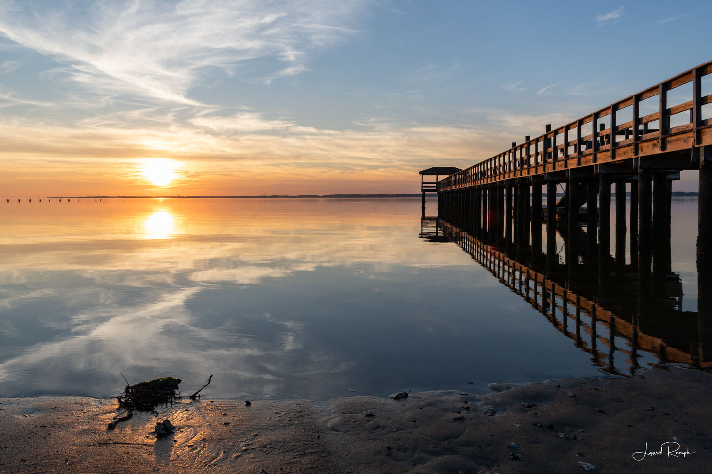 Fort Fisher pier on the Cape Fear River in North Carolina at sunset with calm, glassy water reflecting the pastel sky.