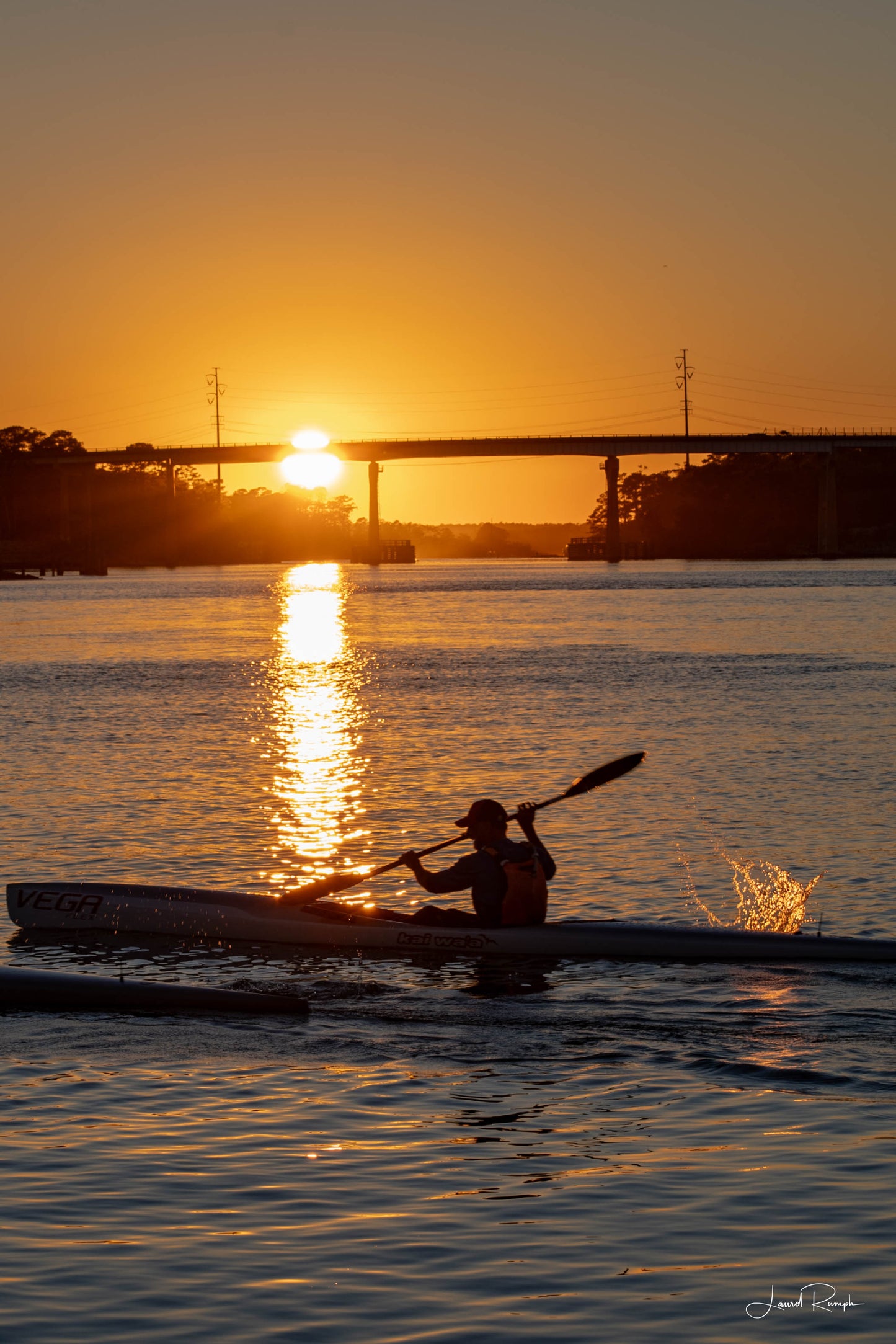 Kayaker at Snow’s Cut Marina, North Carolina with sunset behind Snow’s Cut Bridge and water splashing from the paddle.